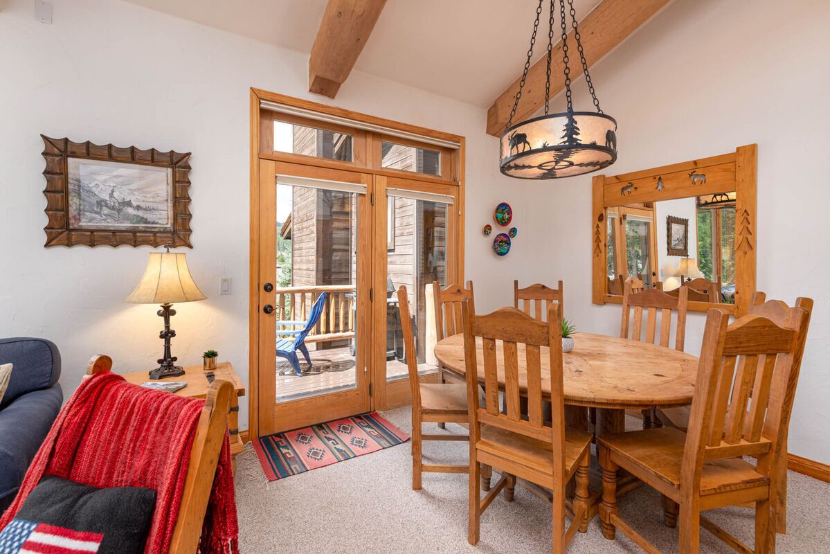 A cozy room with a wooden dining table, chairs, a sofa, a lamp, and a large mirror.