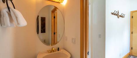 Un baño con un lavamanos blanco, un espejo redondo, un perchero y una puerta de madera.