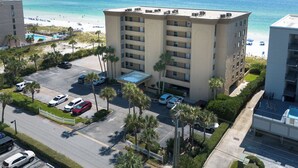 A multi-story hotel with a parking lot, surrounded by palm trees and a view of the beach and ocean.
