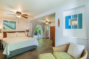 A hotel room with a bed, a chair, a ceiling fan, and a view of the outside.