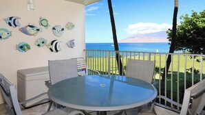 Un balcon avec une table et des chaises en verre, un mur blanc décoré de motifs de poissons et une vue sur l’océan.