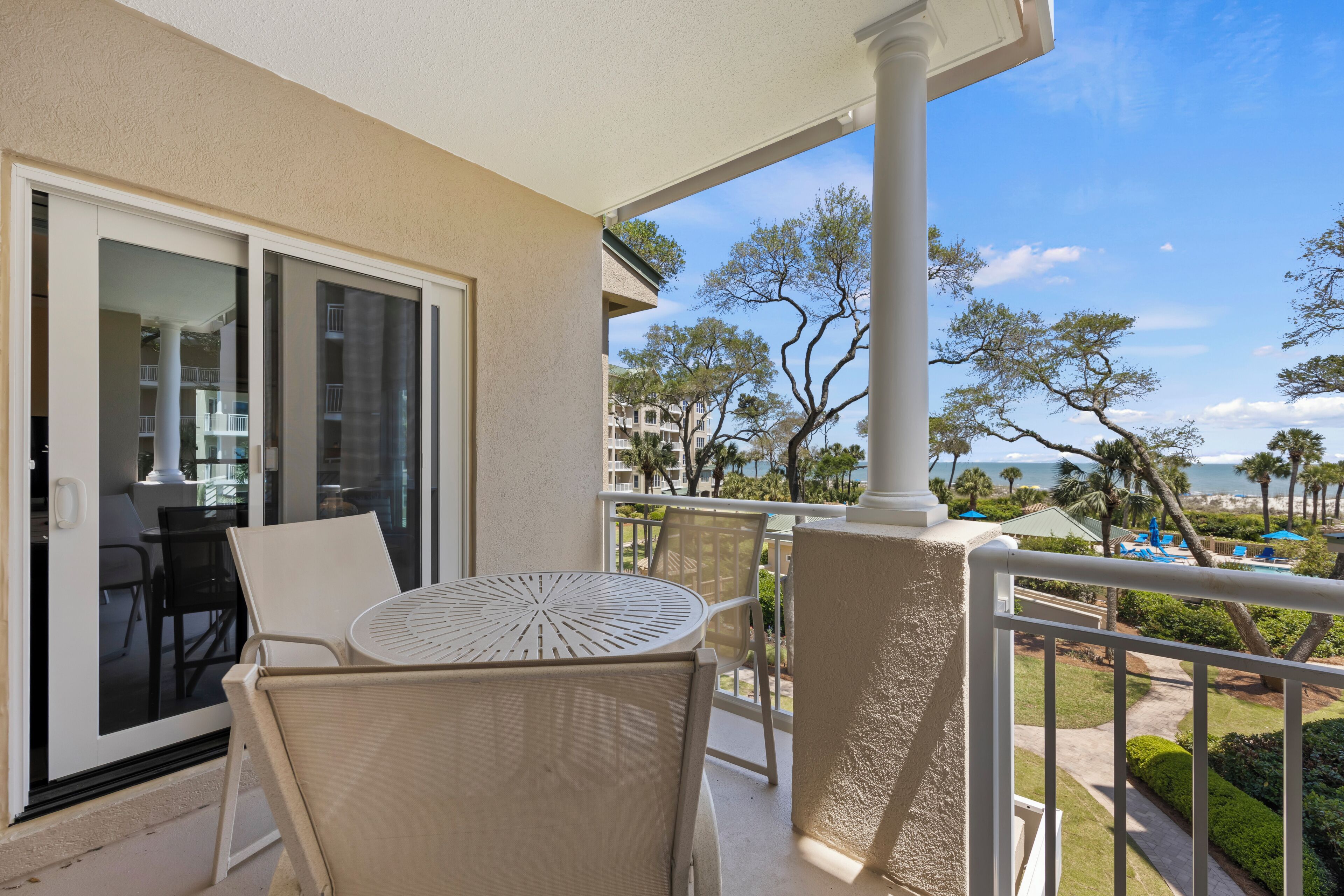 Ein Balkon mit Tisch und Stühlen, einer Glastür und Blick auf Strand und Gebäude.
