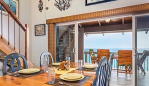 Ein Essbereich mit einem Holztisch, gedeckt für vier Personen, einer Treppe und Blick auf das Meer durch eine Glastür.
