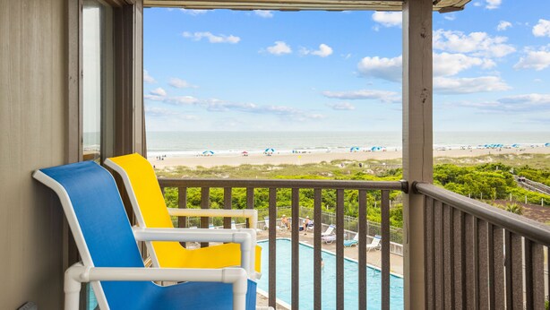 A balcony with a pool view, beach chairs, and a clear sky.