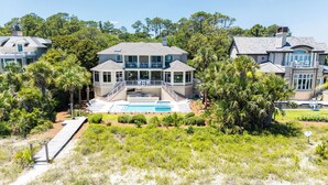 A large, two-story house with a swimming pool, surrounded by lush greenery and palm trees.
