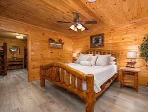 A wooden cabin bedroom with a bed, ceiling fan, and a small bedside table with a lamp. - Free Nights! Unmatched Long Range Views, Hot Tub, Game room. Booking Summer now! (Pigeon Forge)