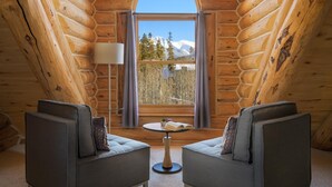 Una habitación tipo cabaña de madera con un ventanal grande, dos sofás, una mesita redonda y una lámpara.