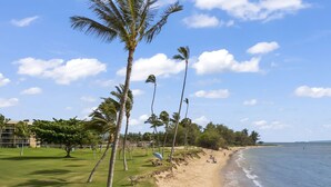 A beach with palm trees, a grassy area, and a building in the background. - Maui Sunset Vacation Rentals B415 (Kihei)