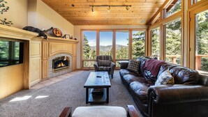 Una sala de estar acogedora con chimenea, sofá de cuero y ventanas amplias que ofrecen vistas al exterior.