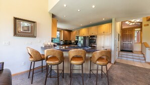 Una cocina con armarios de madera, un refrigerador de acero inoxidable y una zona de bar con cuatro taburetes.