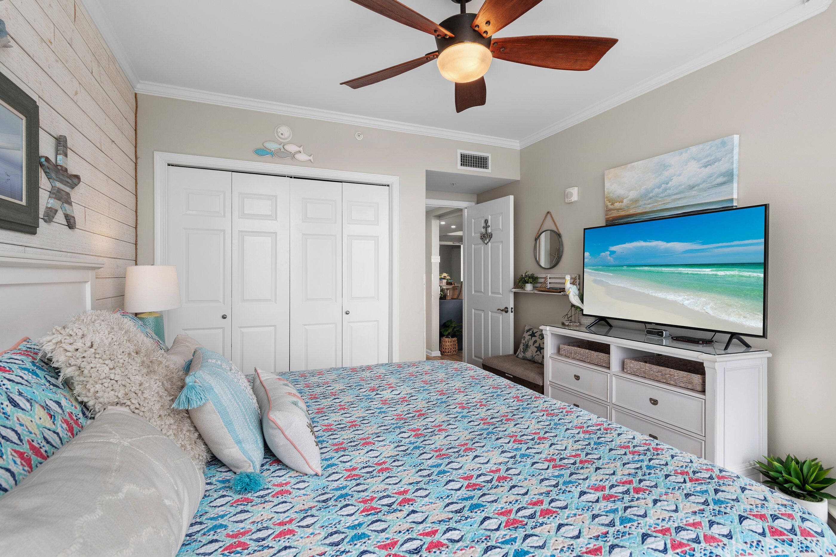 Une chambre à coucher avec un lit, un ventilateur de plafond, une télévision et une porte.