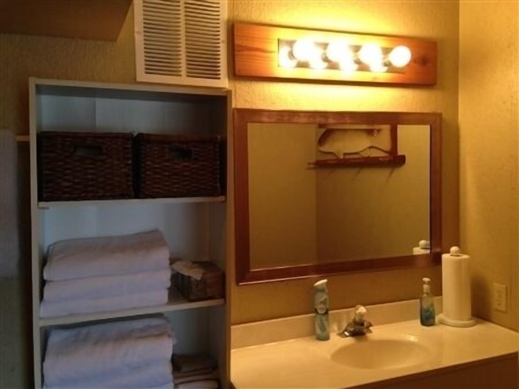 Une salle de bain équipée d’un lavabo, d’un miroir et d’étagères où sont rangées des serviettes et des paniers.