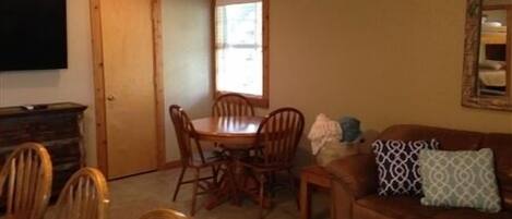 A dining area with a wooden table and chairs, a brown leather sofa, and a window with blinds.