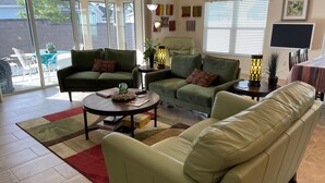 Een woonkamer met een groene bank, een beige bank, een bijzettafeltje, en een eethoek met een tafel en stoelen.