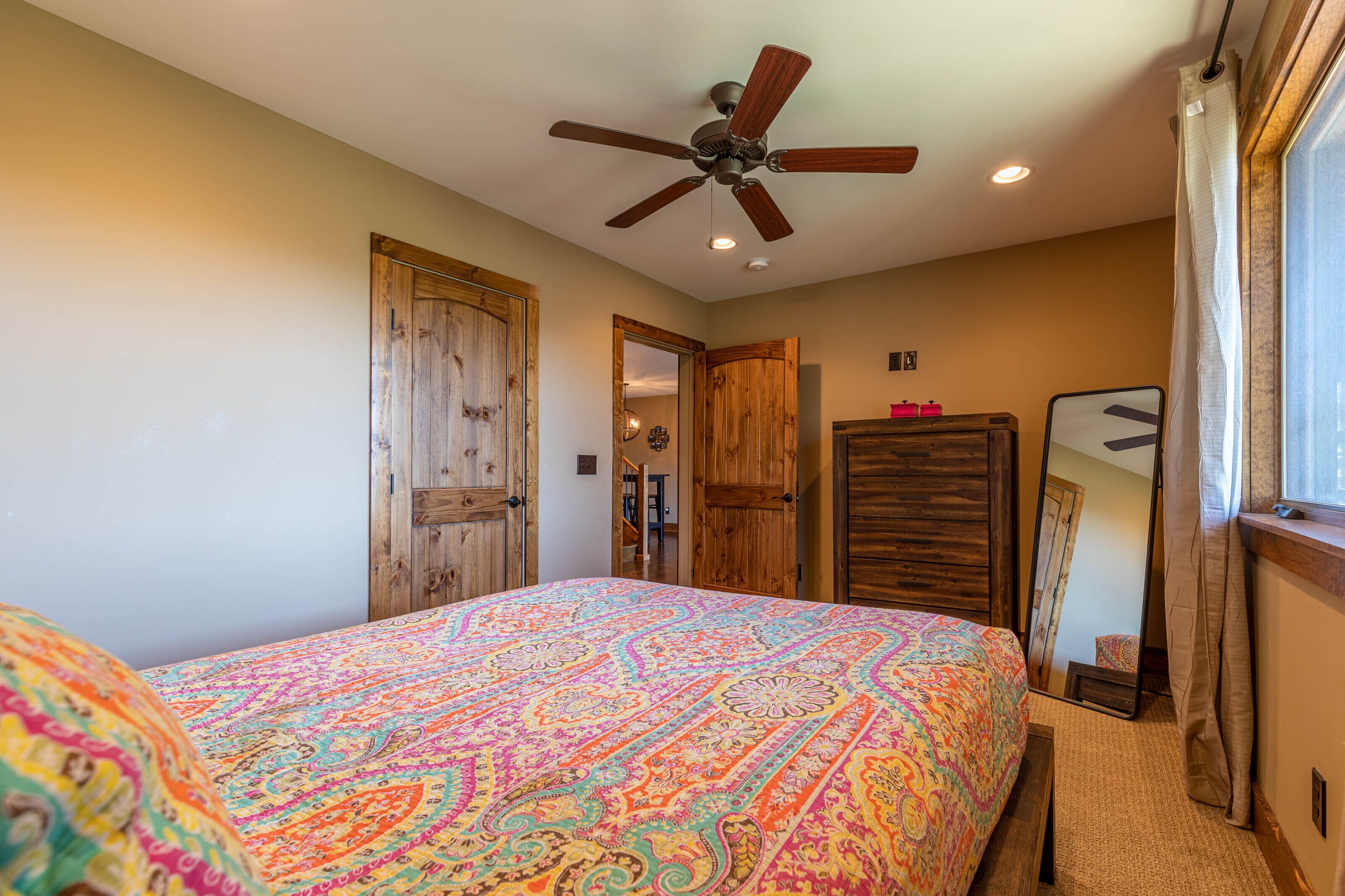 A bedroom with a large bed, wooden doors, a ceiling fan, and a window with curtains.