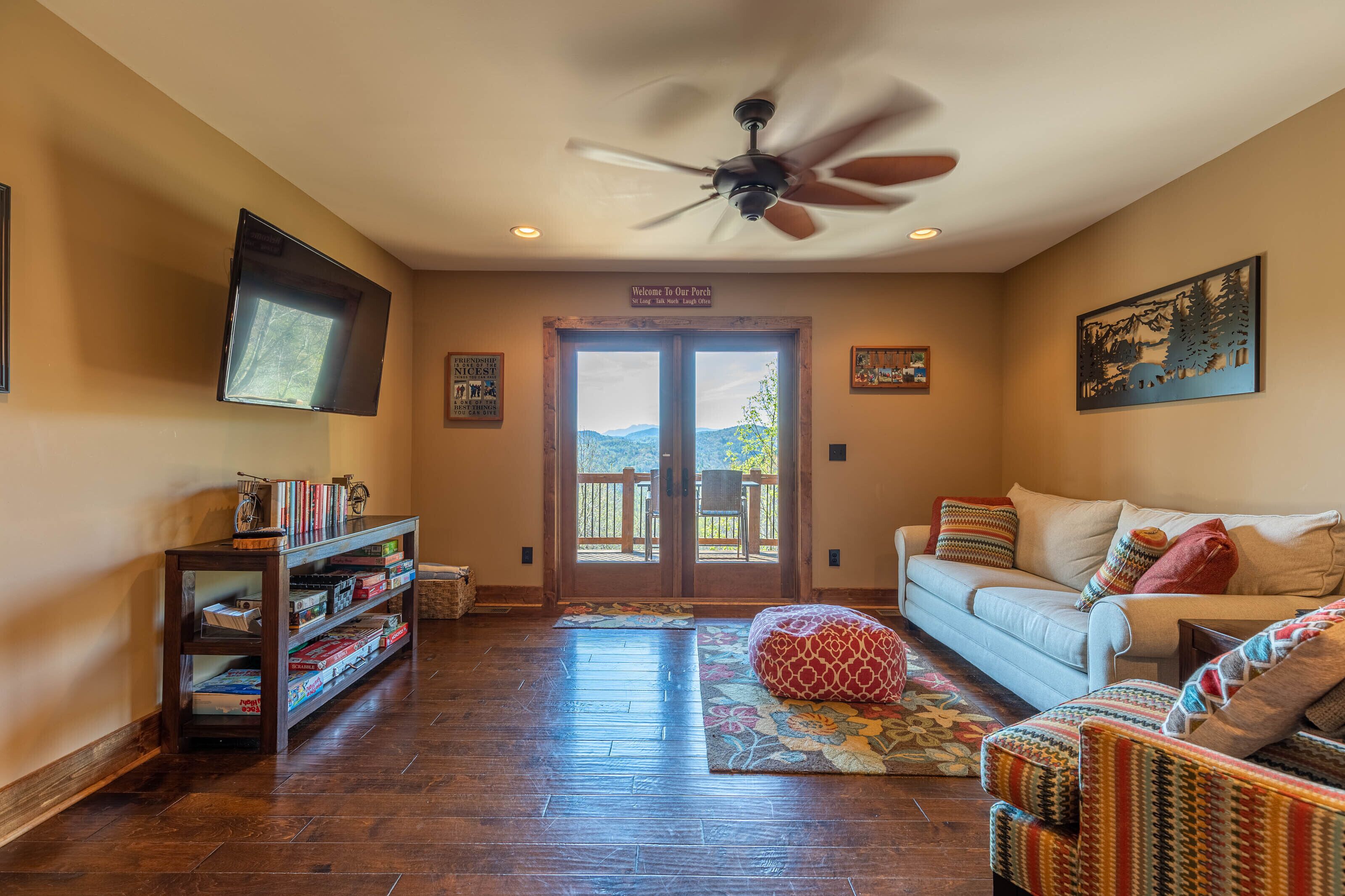 A living room with a sofa, a bean bag, a bookshelf, a flat-screen TV, and a ceiling fan.