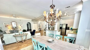 Une cuisine spacieuse avec un îlot central, un coin repas avec une table en bois et des chaises turquoise, et un salon avec un canapé et une table basse.