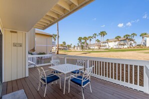 Un espacio al aire libre techado con una mesa y sillas, vista a una playa y palmeras.