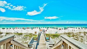 A beach with a wooden boardwalk leading to the water, sandy beach, and umbrellas.