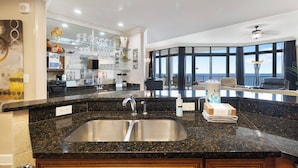 A modern kitchen with a granite countertop, stainless steel sink, and a view of the ocean through large windows. - The Oasis At Orange Beach 2904 by Liquid Life (Orange Beach)