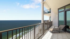 A balcony with a view of the ocean, a lounge chair, and a glass door leading to a balcony with a view of the beach. - The Oasis At Orange Beach 2904 by Liquid Life (Orange Beach)