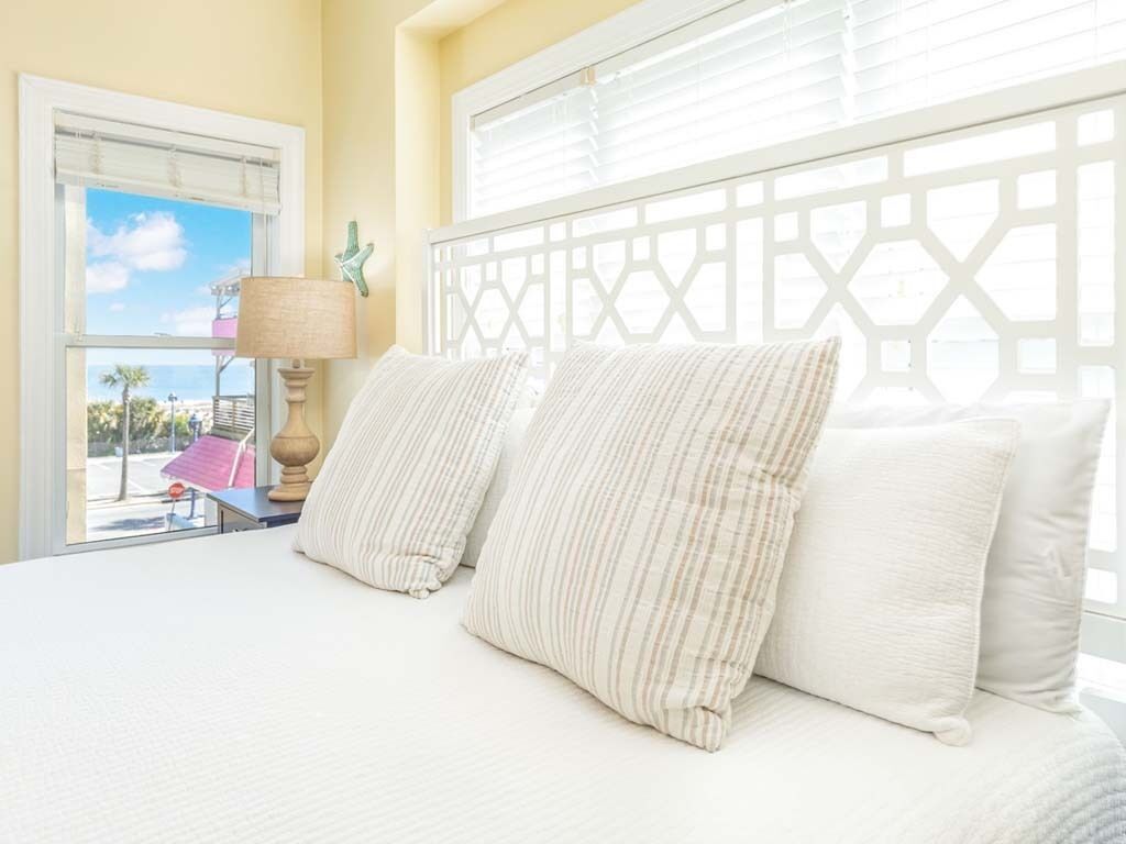 A bed with white bedding and striped pillows, a window with blinds, and a view of the outdoors.