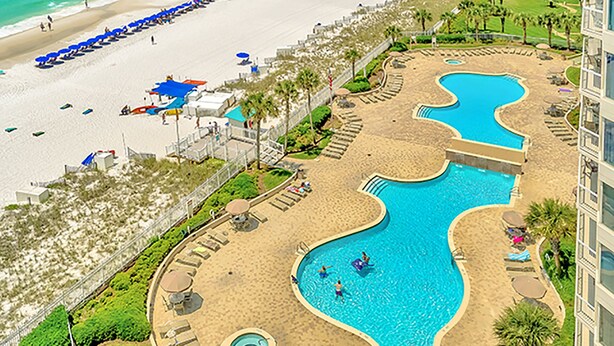Vue aérienne d’un complexe hôtelier doté d’une grande piscine, d’une plage et de nombreuses chaises longues.
