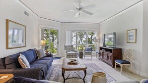 A living room with a sofa, armchairs, a coffee table, a TV, and a ceiling fan. - Great 2 bedroom oceanfront Palmetto Dunes Villa! - Windsor Ct Amenities (Hilton Head Island)