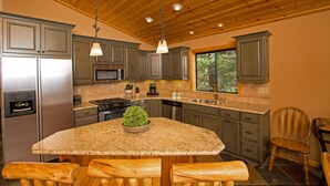 Eine Küche mit Granit-Arbeitsplatten, Holzschränken, einer zentralen Kochinsel mit Pflanze und einer Holzbeschichtung an der Decke.