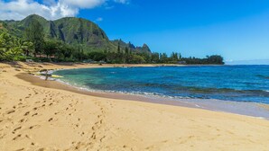 A beach with clear blue water, sandy shore, and a mountain in the background. - Hale Pua Kai, Comfortable Hawaiian Style Home (Haena)