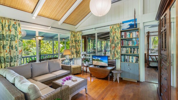 A spacious living room with a large sofa, a television, and a bookshelf. - Hale Pua Kai, Comfortable Hawaiian Style Home (Haena)