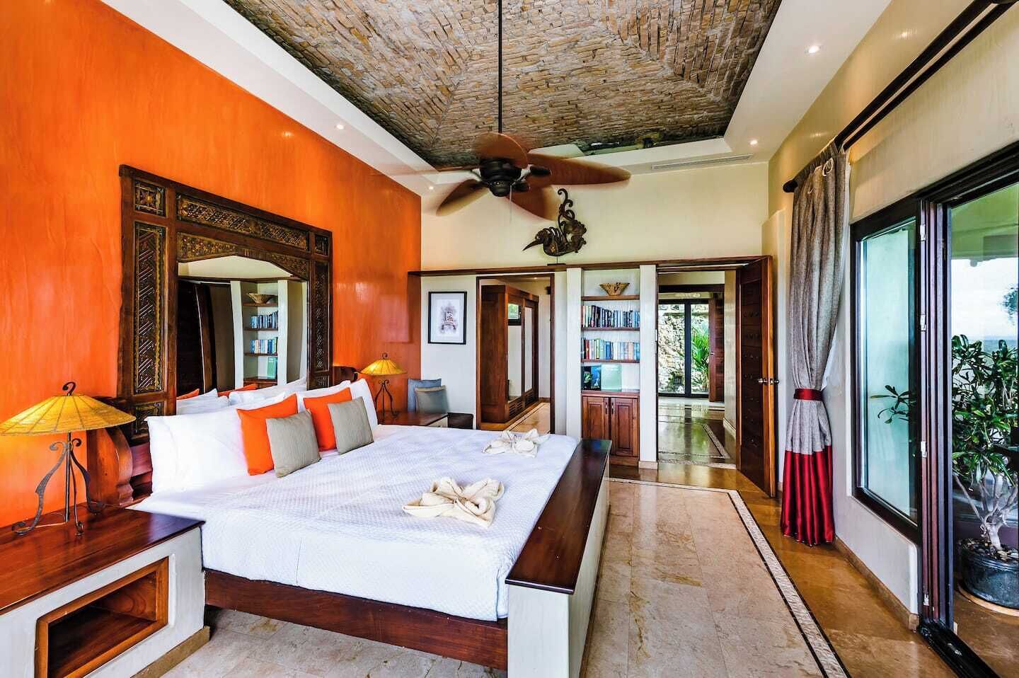 A spacious bedroom with a large bed, a ceiling fan, and a view of the outdoors through a sliding door.