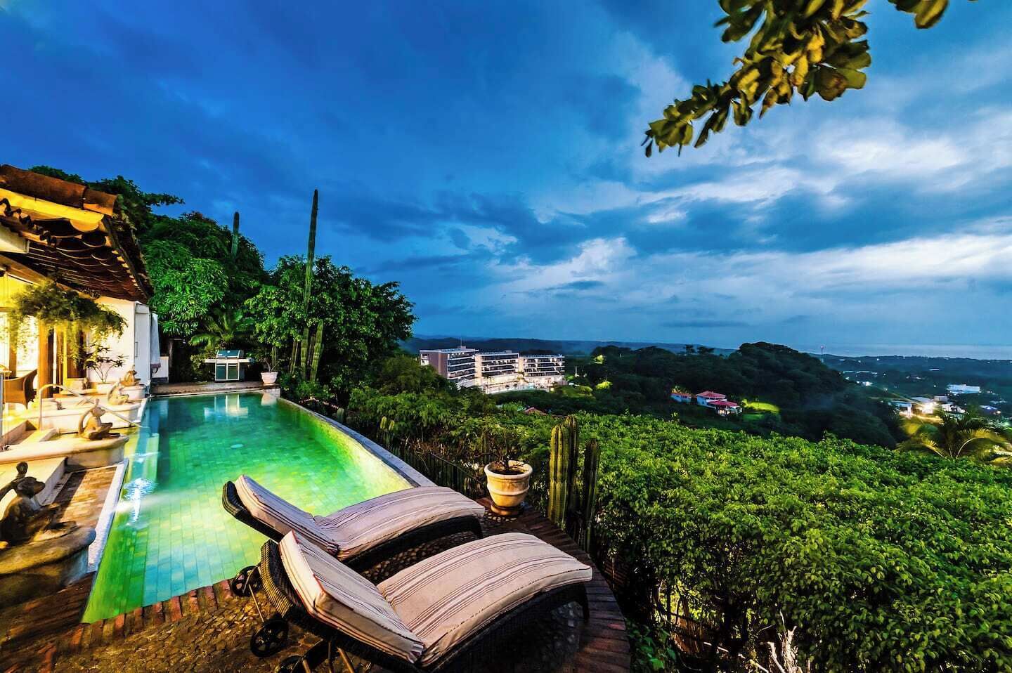 Una piscina con sillas de descanso, vista a un paisaje urbano y un exuberante paisaje verde.
