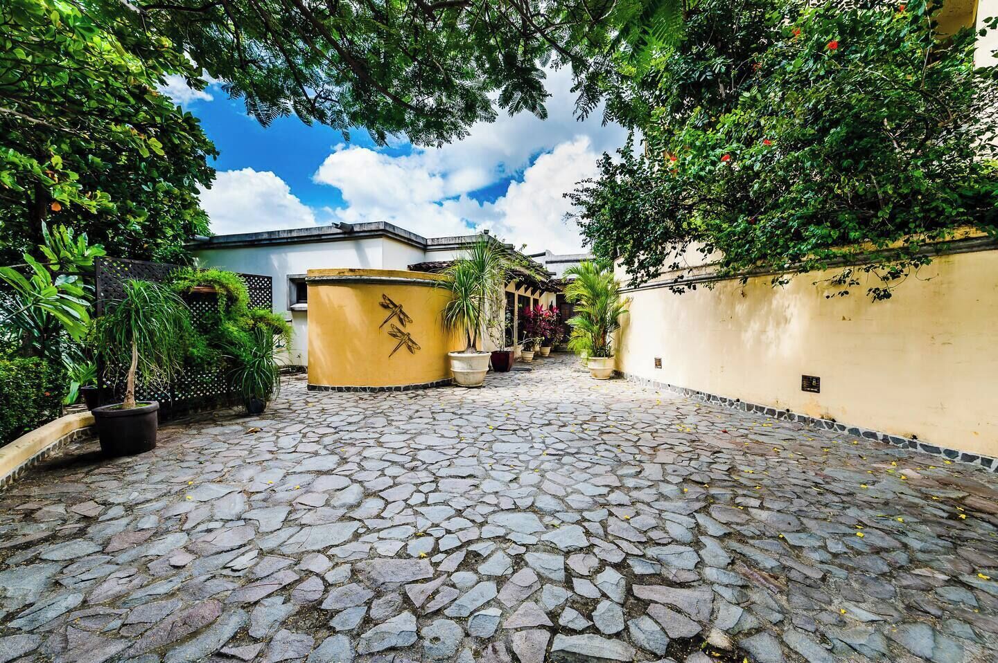 A courtyard with a cobblestone floor, potted plants, and a building with a yellow wall and a dragon sculpture.