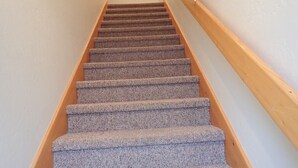 A carpeted staircase with wooden handrails, leading to a landing with a framed picture on the wall. - Spacious 2 Bedroom Apartment above Vacation Home (Almont)