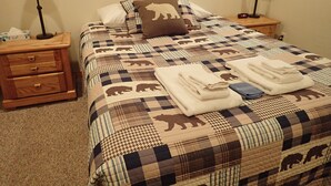 A neatly made bed with a bear-themed quilt, two bedside tables with lamps, and a small wooden nightstand with drawers. - Spacious 2 Bedroom Apartment above Vacation Home (Almont)