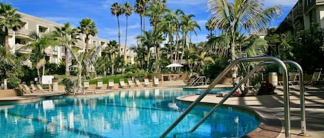 Piscina con sillas de descanso y palmeras, rodeada por un edificio de resort.