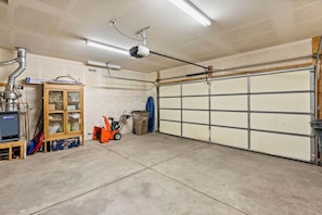 A garage with a concrete floor, a wooden cabinet, a red lawnmower, and a garage door. - Creekside Retreat with Yard, Close to Downtown and Ski, Dog Friendly (Durango)