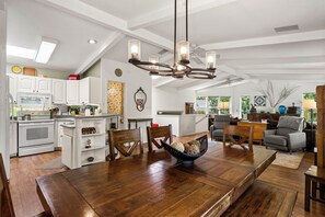 A spacious kitchen with white cabinetry, a dining area with a wooden table, and a living room with a gray sofa.