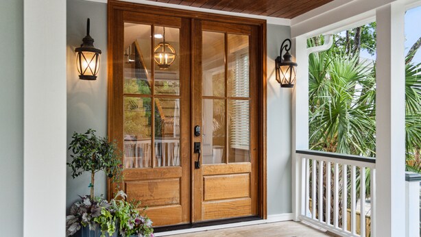 A wooden front door with glass panels, two wall-mounted lanterns, and a potted plant on the porch. - Luxury Vaycay! Private Pool, Billiards, Hot Tub, Putting Green - 2602 Hartnett (Isle of Palms)