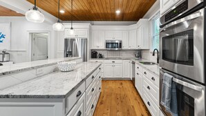 A modern kitchen with white cabinets, stainless steel appliances, a wooden ceiling, and a marble countertop. - Luxury Vaycay! Private Pool, Billiards, Hot Tub, Putting Green - 2602 Hartnett (Isle of Palms)