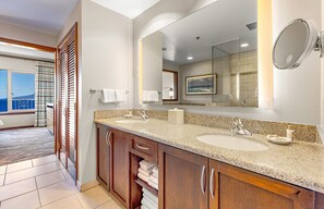 Une salle de bain d’hôtel avec deux lavabos, un grand miroir et une vue sur la mer par la fenêtre.