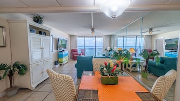 A spacious living area with a balcony overlooking the sea, furnished with a dining table, chairs, and a sofa.