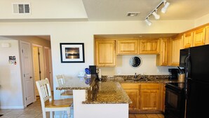 A kitchen with wooden cabinets, a granite countertop, a black refrigerator, and a dining area with white chairs. - Wild Card by Mesquite Vacation Rentals: Pet Friendly with Community Amenities and $510 in free daily activities (Mesquite)