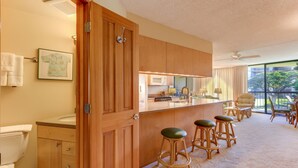 A kitchen with wooden cabinets, a microwave, and a bar area with stools. - Maui Sunset Vacation Rentals A-306 (Kihei)