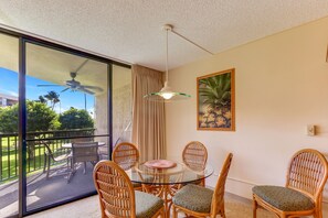 A balcony with a glass table and wicker chairs, a ceiling fan, and a painting on the wall.