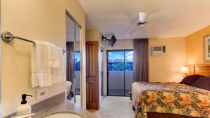 A hotel room with a bed, a bathroom with a sink and towel rack, a ceiling fan, and a view of the outdoors. - Maui Sunset Vacation Rentals A-306 (Kihei)