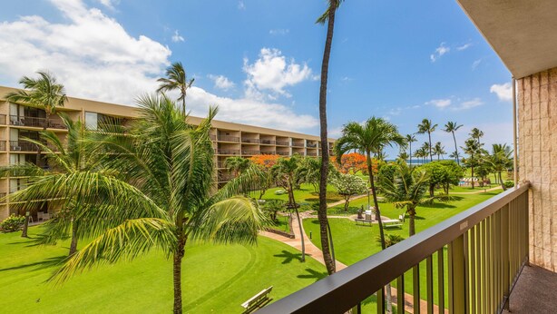 A hotel with a balcony overlooking a well-maintained lawn and palm trees. - Maui Sunset Vacation Rentals A-306 (Kihei)