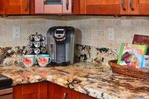 A kitchen with a coffee maker, a fruit bowl, and a basket of cookbooks.