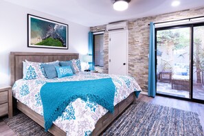 Een slaapkamer met een groot bed, een nachtkastje, een lamp, een ingelijst schilderij aan de muur, en een schuifdeur naar een buitenruimte.